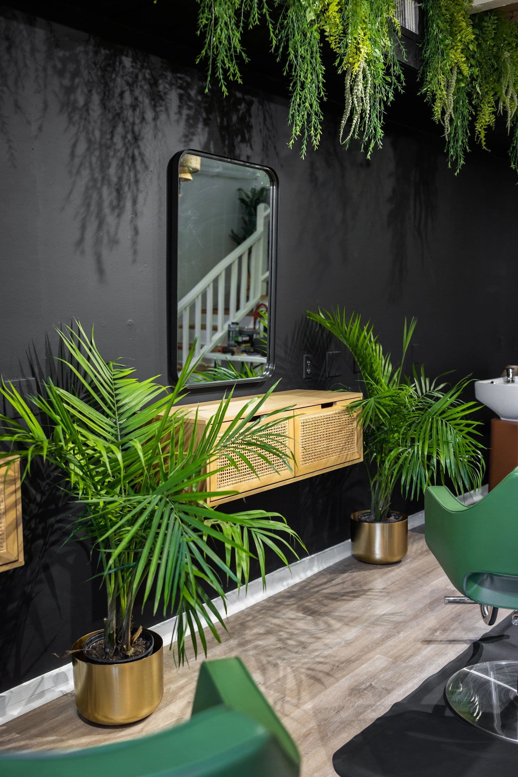 Styling station with mirror and lush tropical plants against dark wall