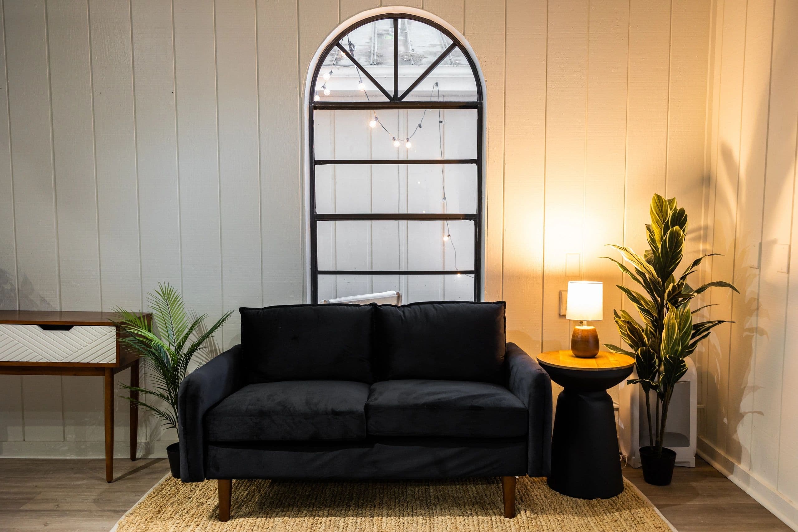 Waiting area with black velvet sofa, arched mirror, and warm lamp lighting