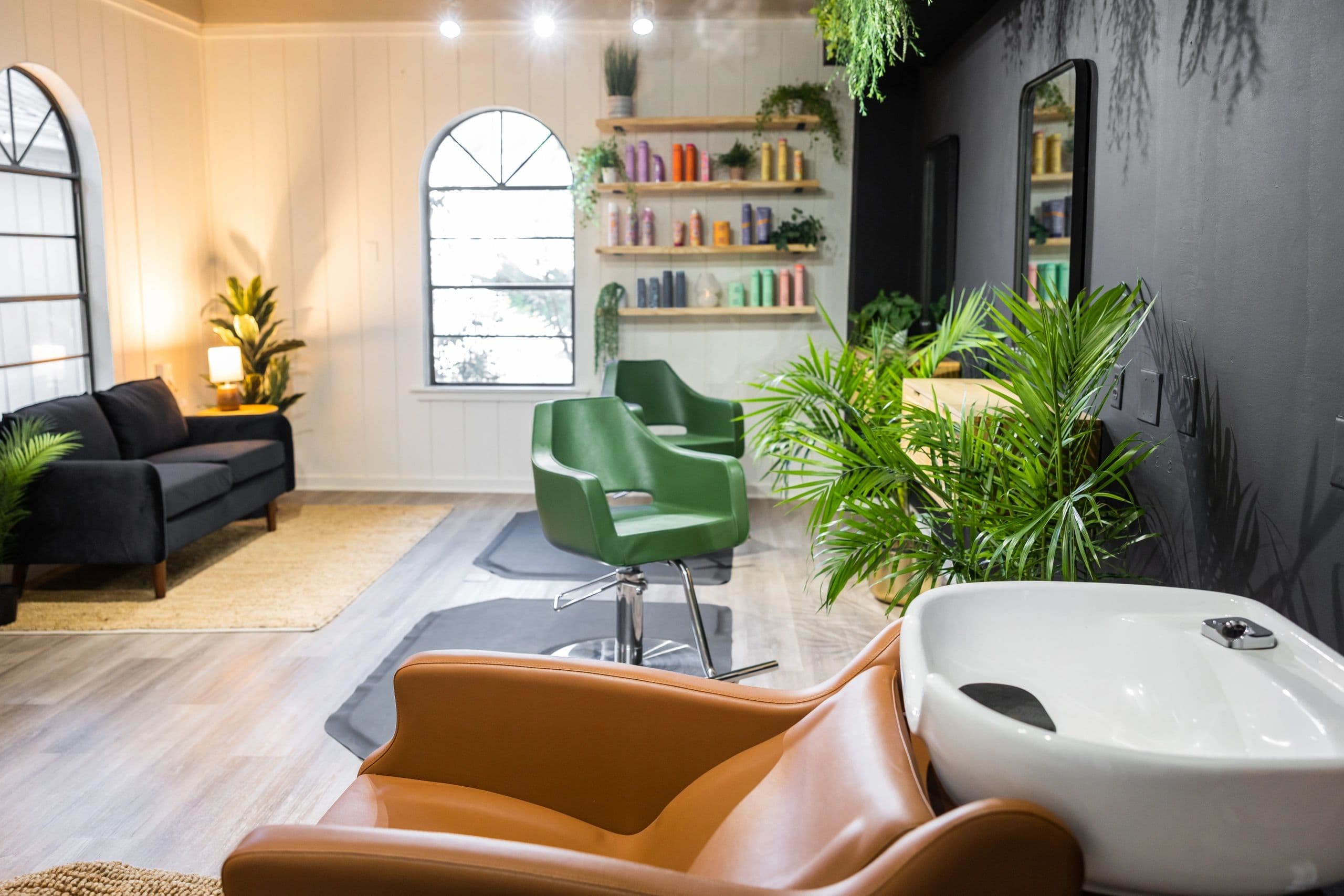 Full salon view with styling chairs, wash basin, product display, and plants
