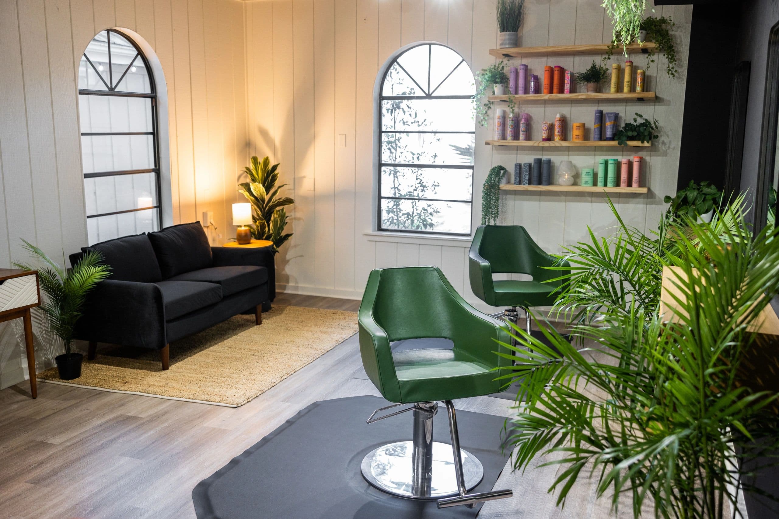 Salon interior with green styling chairs, colorful product shelves, and cozy lounge seating