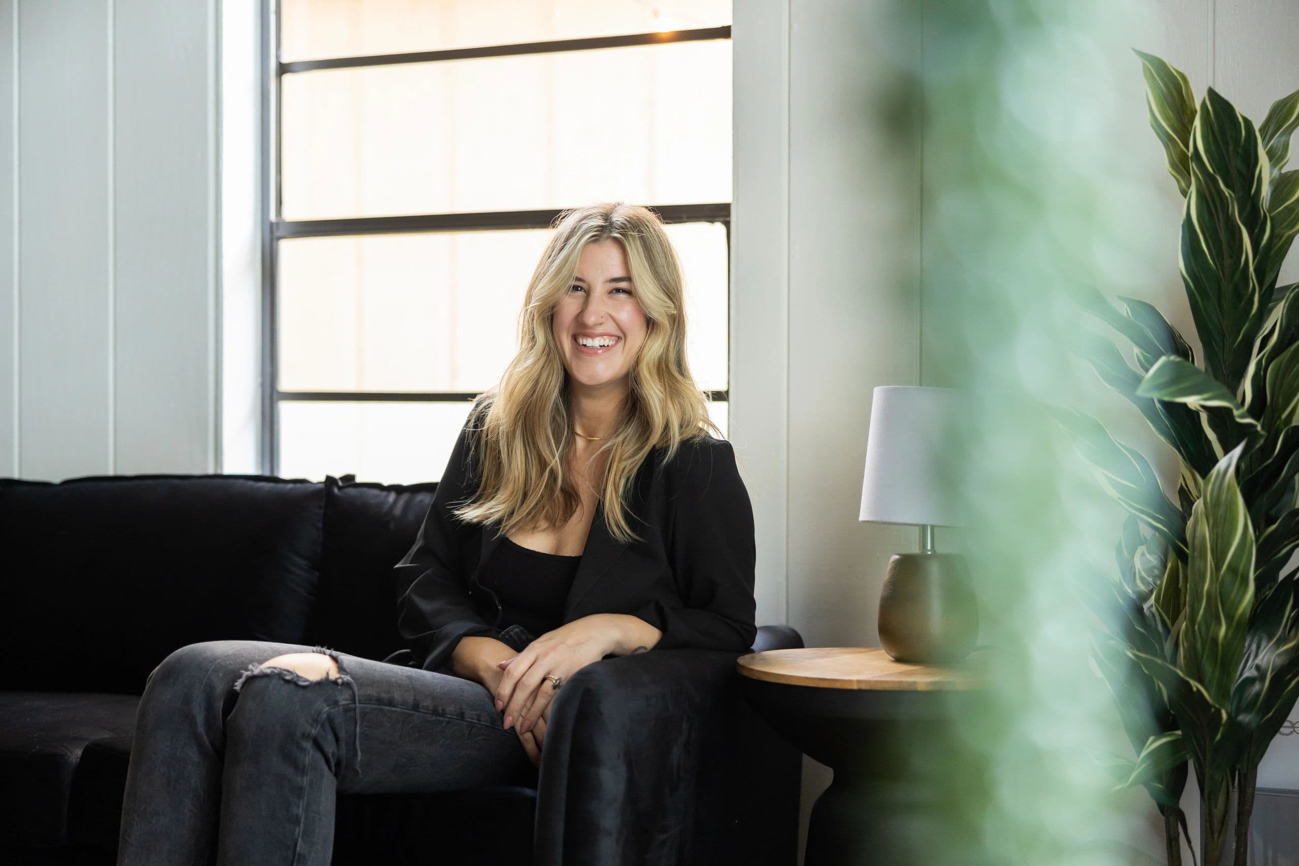 Salon owner smiling on the lounge sofa by a sunlit window